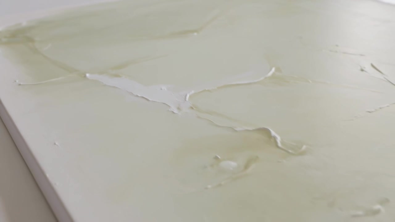 Spreading pale liquid, corner smear starting flow across rigid panel in studio white ridge forming