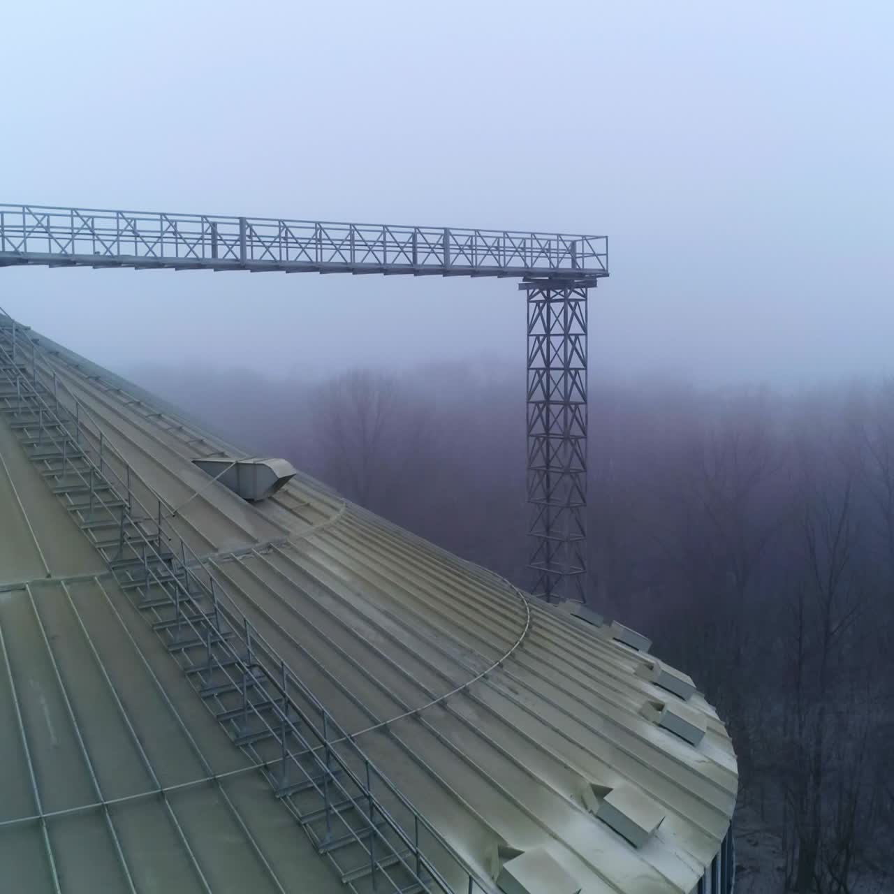Dusty top of a huge silo tank at modern elevator. Drone shot slow motion over the silver granary tank on winter foggy weather