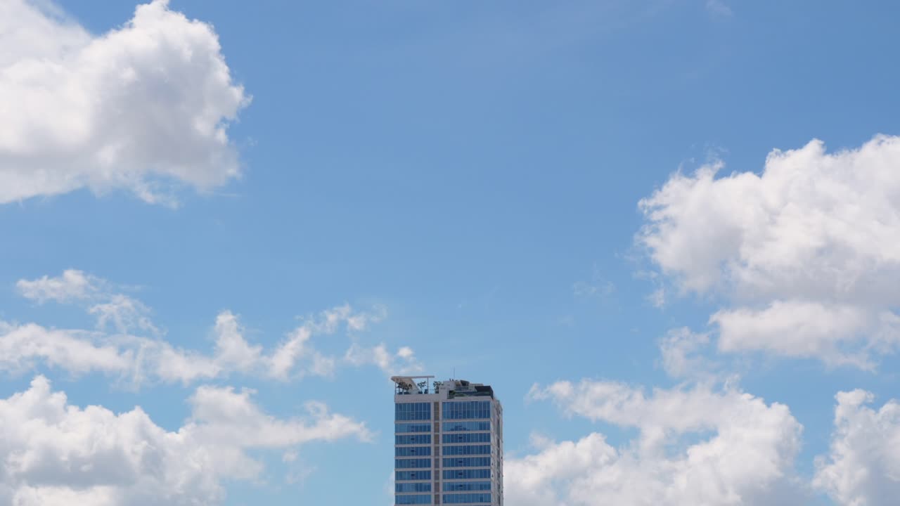 Time-lapse clouds moving above tall commercial building skyscraper real estate