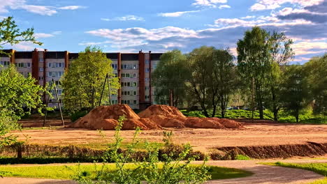 mounds of dirt beside apartment blocks with trees glowing in evening sunlight