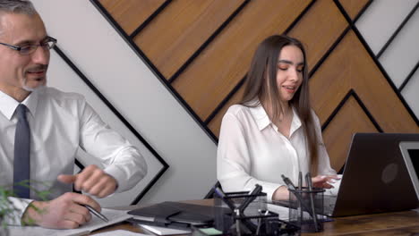 mature man helping her female co worker with the computer