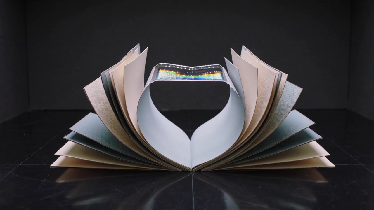 Motore che solleva le pagine di un libro rilegato, formando un cuore che si innalza a corona in uno studio con una striscia lucida che modella le forme.