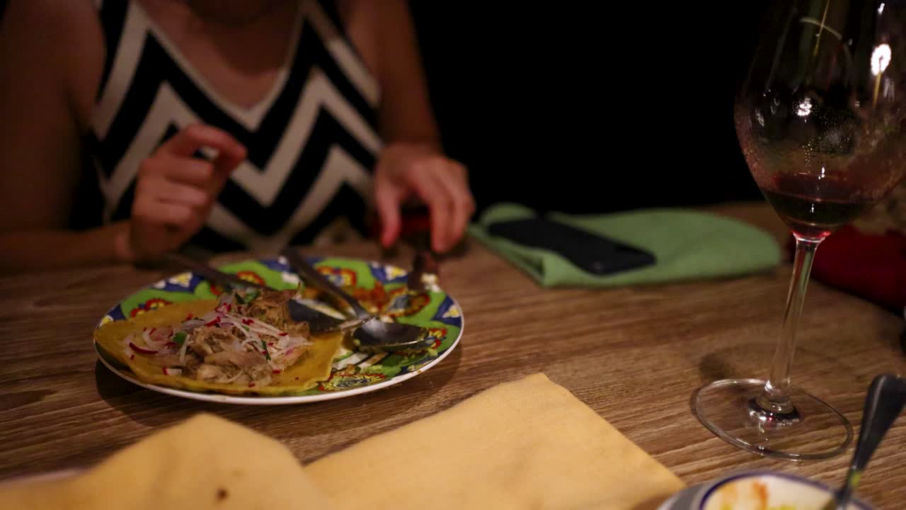 A person enjoys a Mexican meal with wine in a cozy setting, featuring warm lighting and casual ambiance