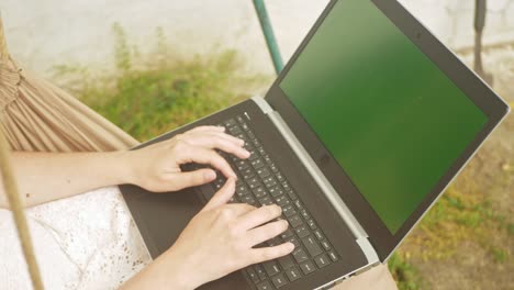 woman rides on a swing and communicates with friends using a laptop. green screen, rest in the yard of the house. outsdoor. social networks, the internet, messages. in nature. close up