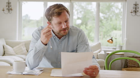 worried man sitting at table at home reviewing domestic finances looking at bill