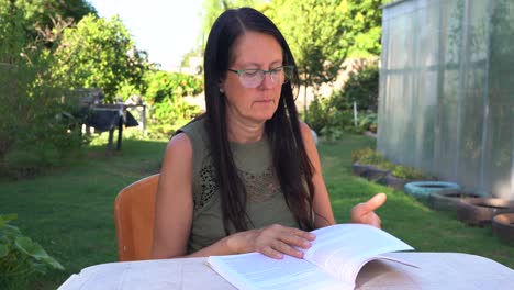mujer de mediana edad leyendo un libro en el patio trasero de su casa