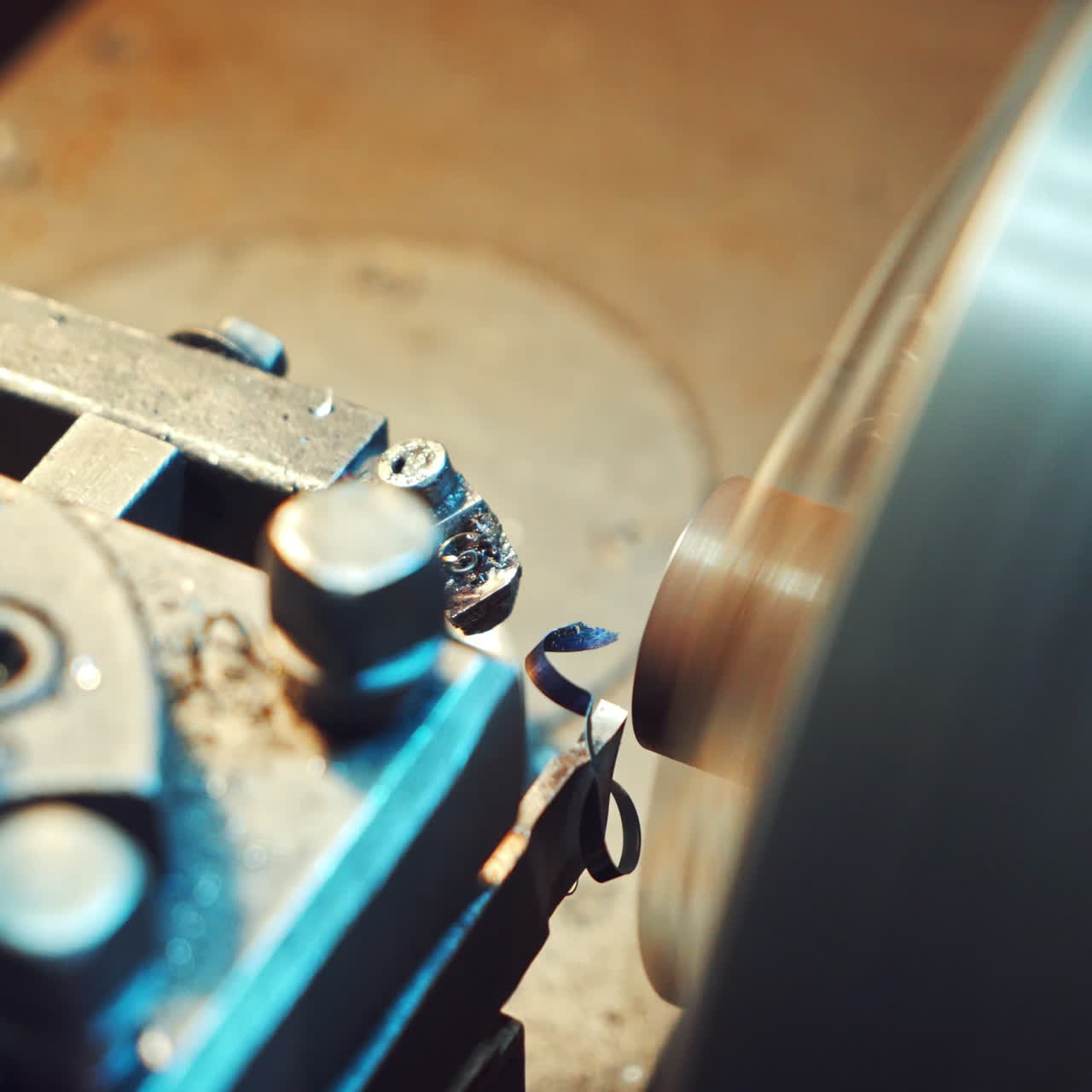 A cutter of lathe is sharpening metal billet for production at the plant. Thin shavings are falling on the surface of the equipment. Close-up.