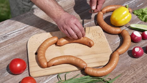 mans hands cutting barbeque sausages. cutting ingredients for picnic.