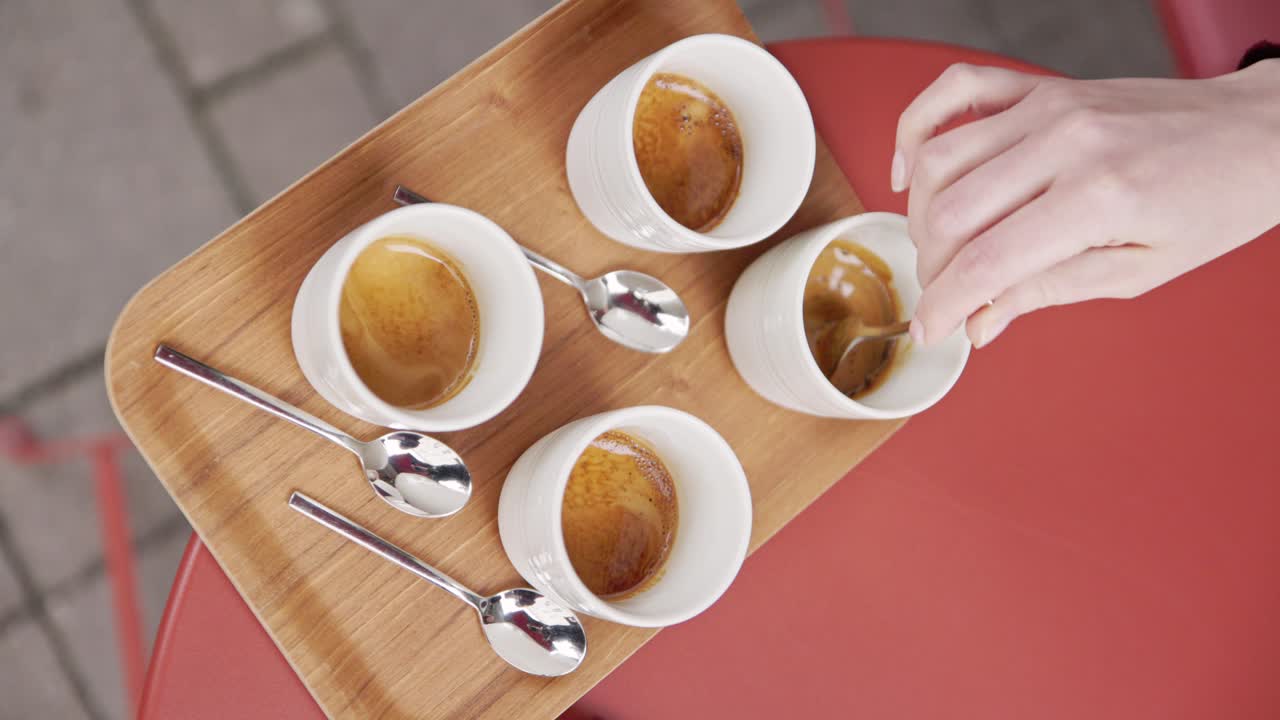 Vertical, hand stirs coffee with spoon in white cup on wooden tray and red table