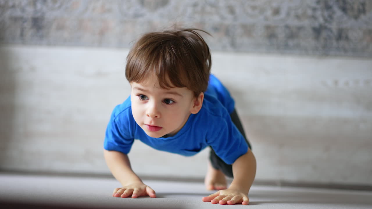 Two-year old toddler standing at the wall trying to climb it. Kid fail and sits on the floor. Close up. Top view.