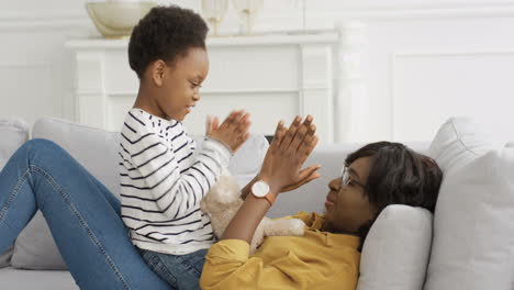 Madre-Feliz-Jugando-Al-Juego-De-Manos-Con-Una-Pequeña-Y-Linda-Hija-En-El-Sofá-De-Casa