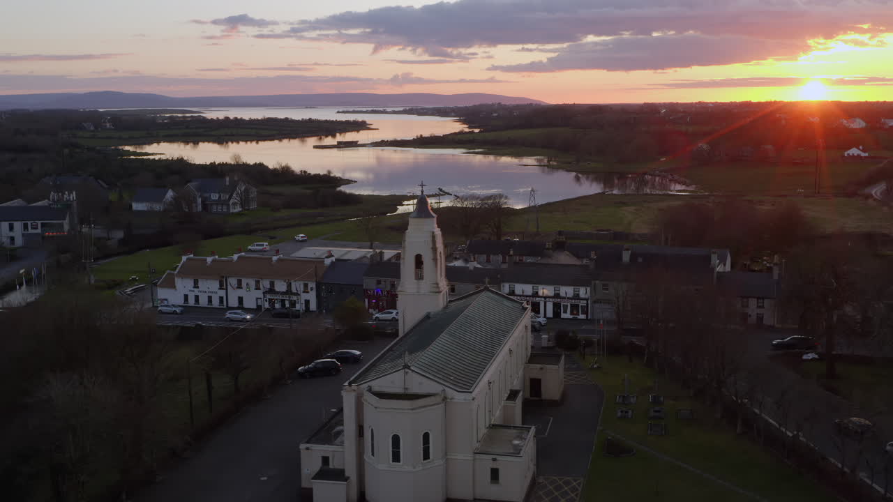 Slow motion approach to backlit church as sunlight fades over Clarinbridge rooftops and evening sky tones