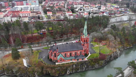 dolly out aerial view of distinctive neo gothic style trollhättan church located on cliff in göta river, västra götaland county sweden