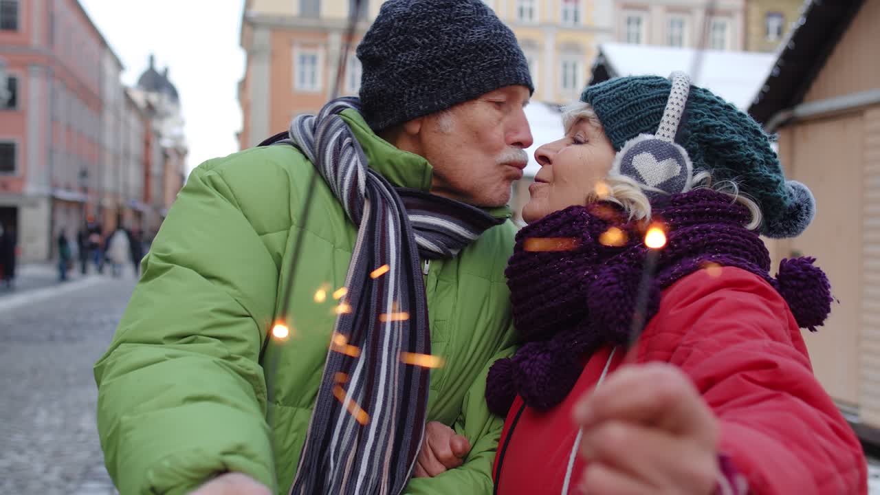 una pareja de ancianos con luces bengalíes disfrutando de la víspera de navidad, besándose en la ciudad de invierno
