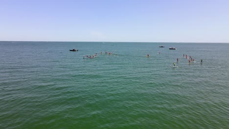 Vista-Aérea-Deslizante-Que-Muestra-El-Evento-De-Carrera-De-Paddle-Surf-De-Pie-En-Las-Aguas-De-La-Playa-De-Rexhame,-Marshfield