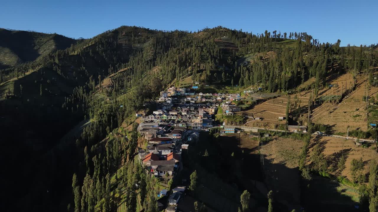 Aerial drone footage of countryside mountain settlement in Indonesia surrounded by fields and dense trees