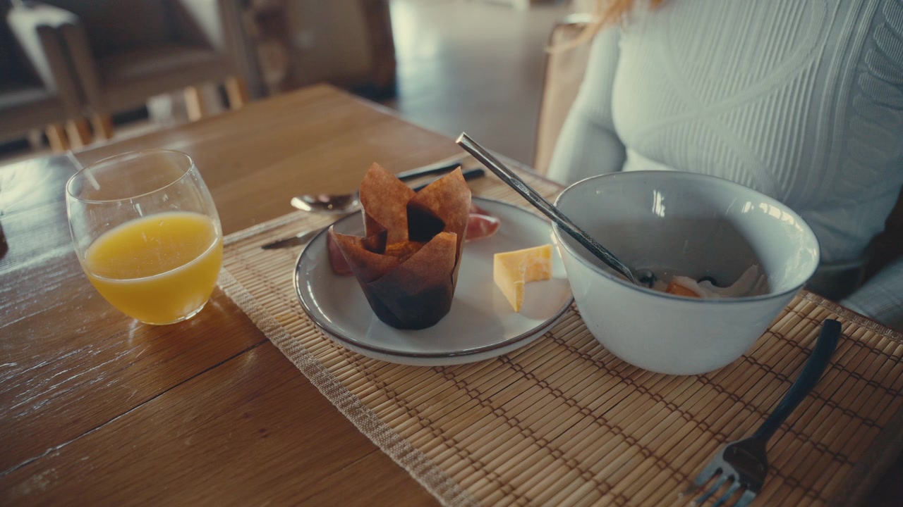 Primo piano di una donna che fa colazione e si alza dal tavolo, angolazione statica a ¾ di una varietà di cibo in 4k.
