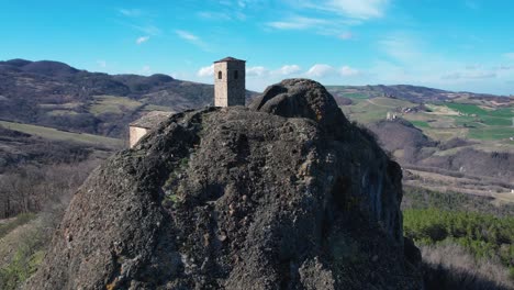 aerial footage of pietra perduca, volcanic rock, church set at top stone immersed in countryside landscape, cultivated land in val trebbia bobbio, emilia romagna, italy