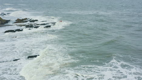 Vista-Aérea-De-Las-Olas-Rompiendo-Contra-Las-Rocas-A-Lo-Largo-De-La-Costa-Durante-Una-Tormenta