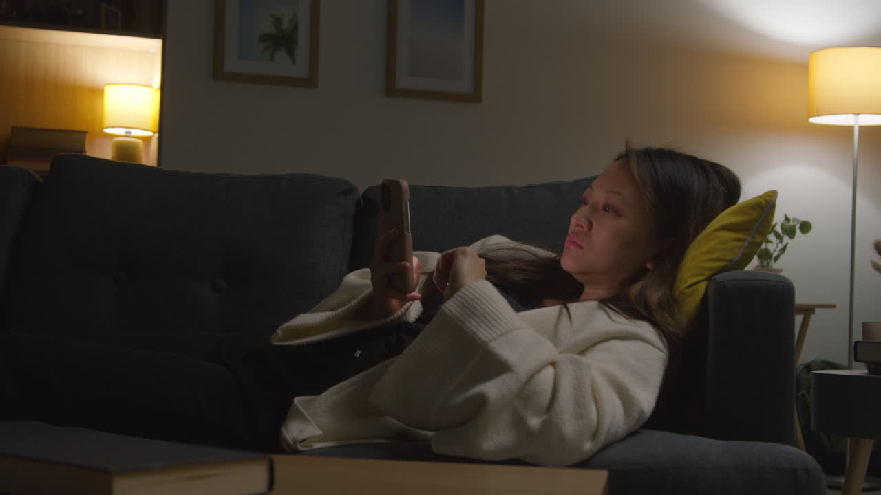 mujer que pasa la noche en casa acostada en el sofá con el teléfono móvil explorando internet o las redes sociales 2