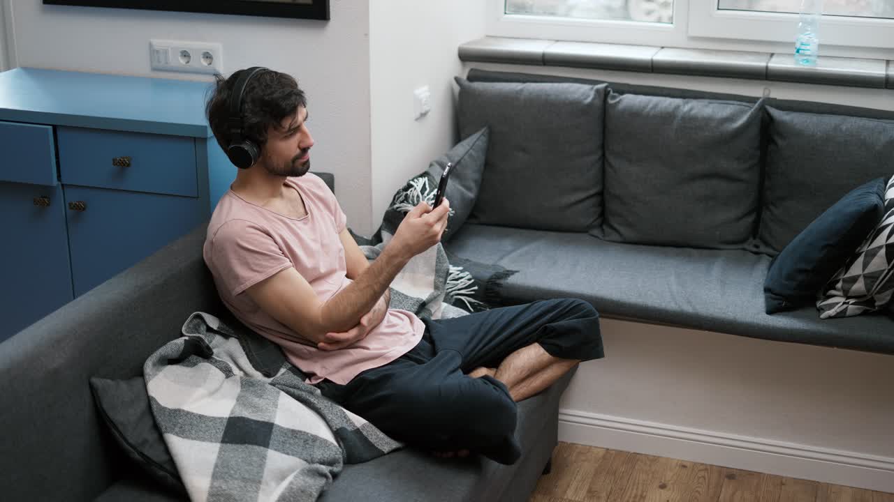 vista de alto ángulo de un joven caucásico escuchando música en auriculares, desplazándose en el teléfono inteligente en casa