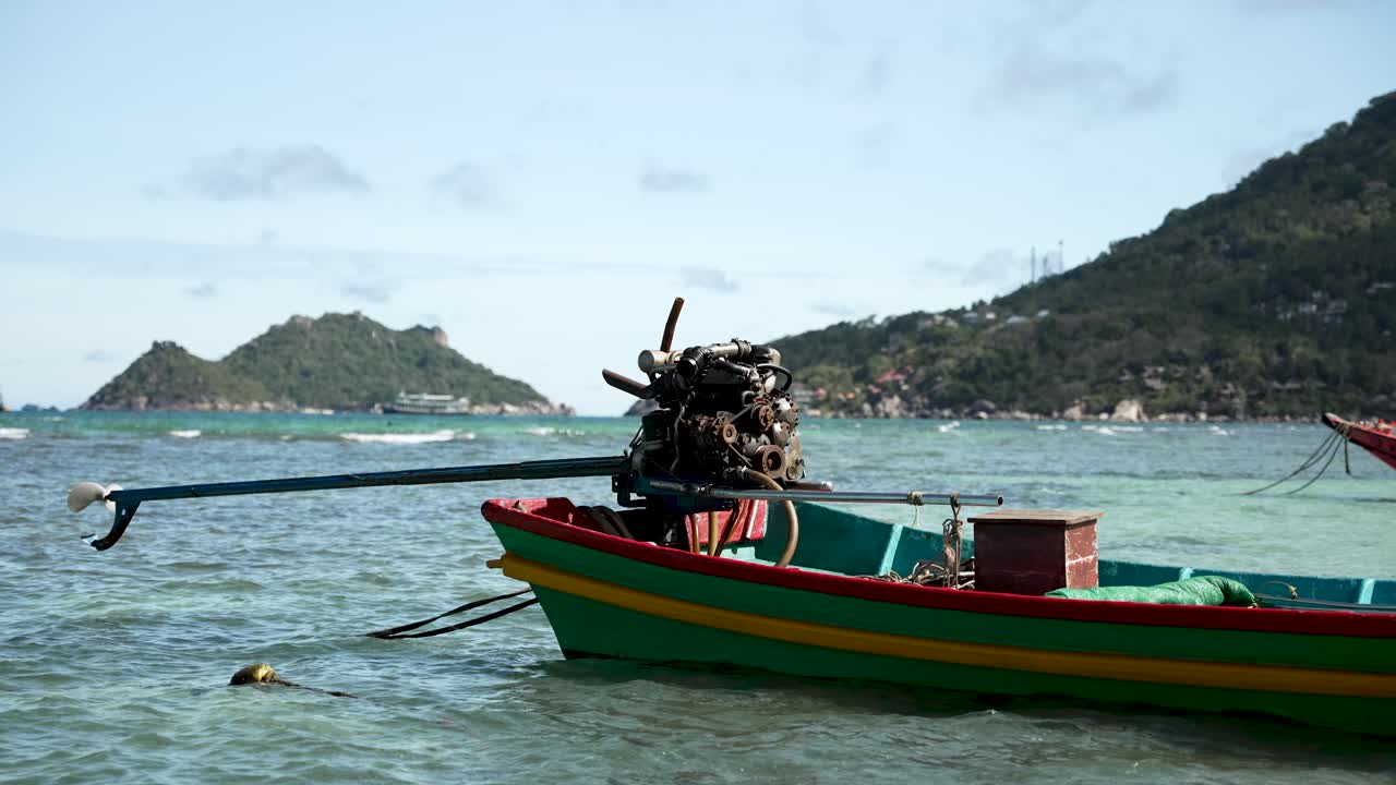 un barco vibrante y colorido con un motor visible está anclado en las aguas claras y turquesas cerca de un paisaje de isla exuberante y verde bajo un cielo brillante con algunas nubes