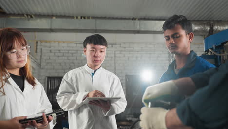 mechanic in white gloves demonstrates spanner use to attentive students in automotive workshop, students in lab coats observe and take notes while surrounded by tools and equipment