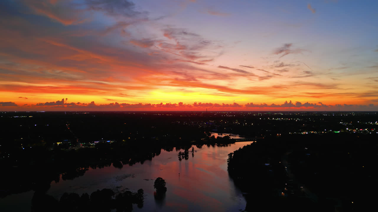 Orange pink sky over forest and lake, drone dolly of glowing reflections during sunset with sparkling home lights, backdrop background