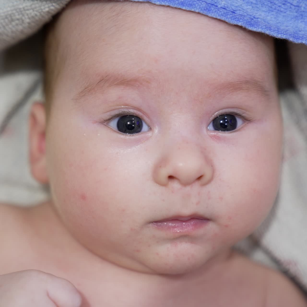 Beautiful kid looking in front of him, lying calmly and peacefully. Baby boy covered in bath towel after washing time. Close up