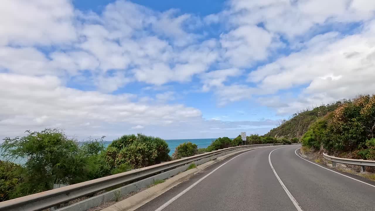 A 13-second video captures a drive along the Great Ocean Road, showcasing coastal views, lush greenery, and a winding road under a partly cloudy sky