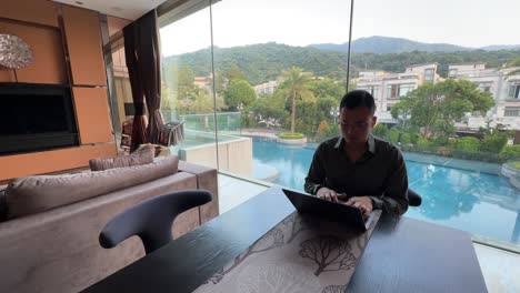 wealthy asian millennial entrepreneur man typing on laptop in luxury living room