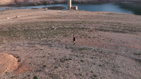 aerial drone circling around man walking into drought area in water reservoir