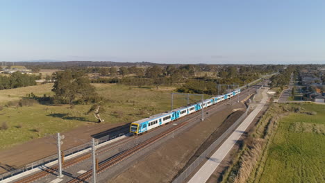 Aerial-chase-shot-following-train-as-it-arrive-at-elevated-station-over-skatepark-beneath