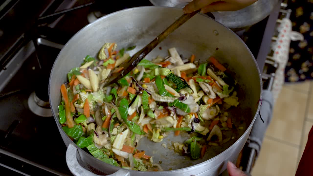 A cooking chef mixes vegetable stir-fry with a wooden spoon in pot, embodying the essence of culinary preparation and food crafting