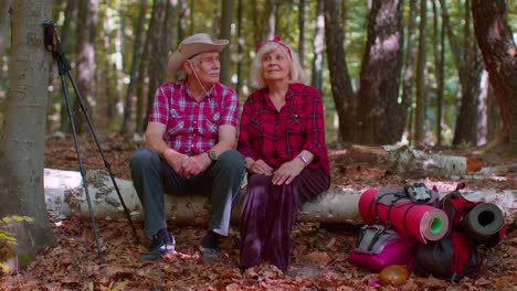 Grandmother-grandfather-senior-tourists-hikers-sitting-on-tree-and-hugging,-kissing-in-summer-forest