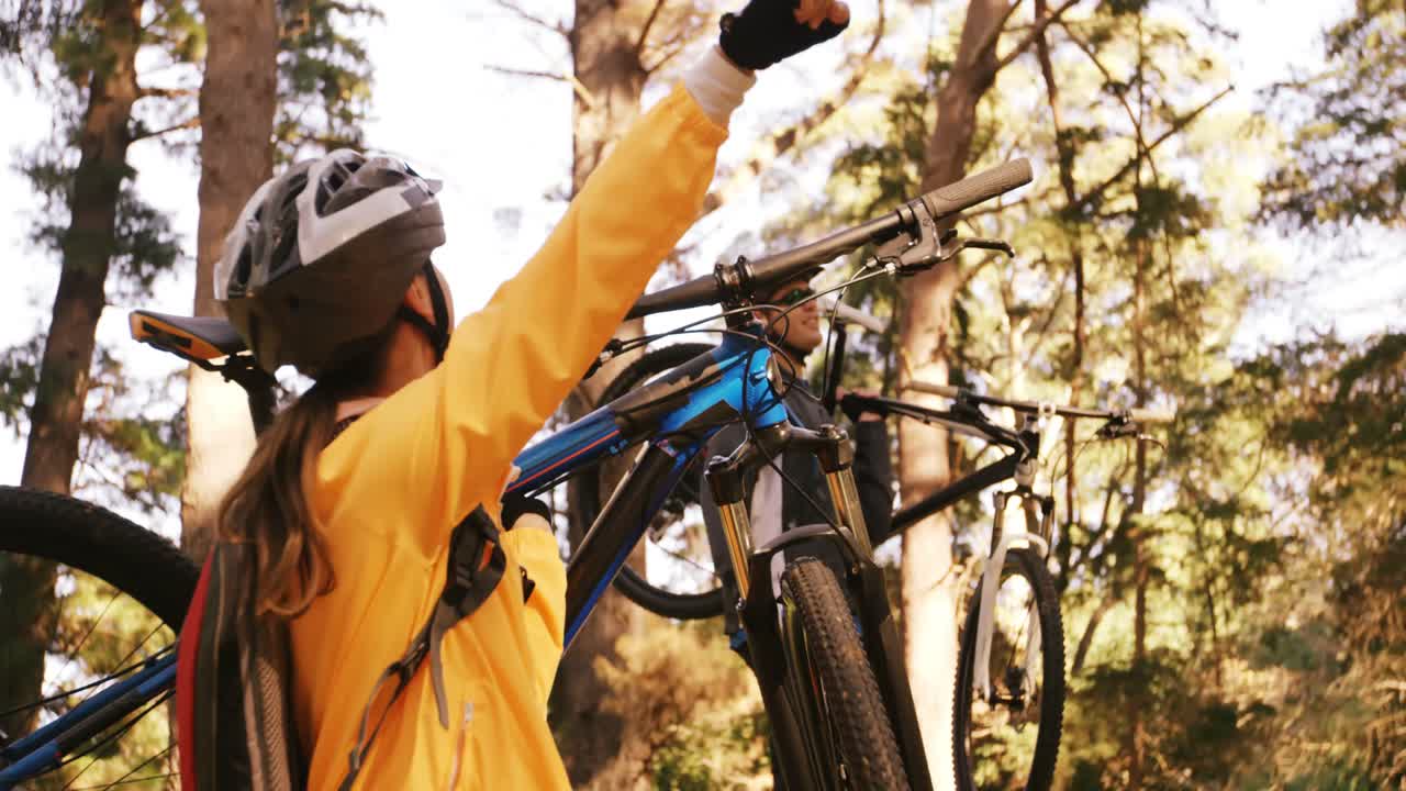 pareja de ciclismo de montaña llevando una bicicleta y apuntando a la naturaleza