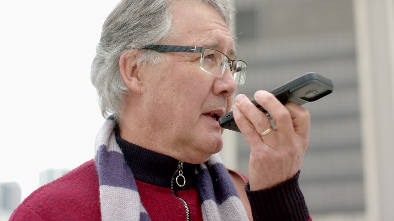 Senior man raising handheld device and speaking into it to communicate update on urban rooftop