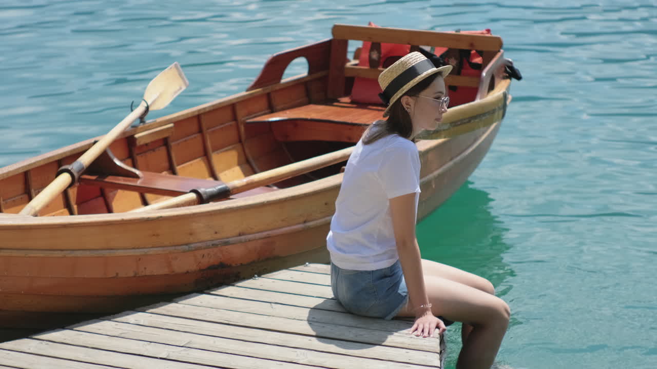 mujer relajándose en un muelle por un barco de madera en un lago
