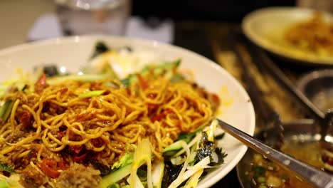 close-up of chopsticks lifting noodles from a colorful dish with vegetables and sauce.