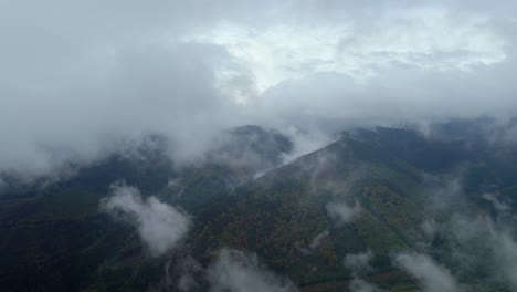 Aerial-drone-forward-moving-shot-over-white-clouds-passing-by-over-mountain-range-covered-with-dense-green-vegetation-at-daytime