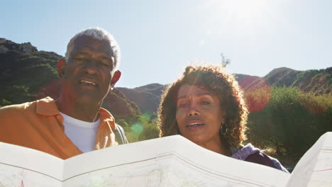 una pareja de ancianos afroamericanos mirando el mapa mientras caminan juntos por el camino en el campo