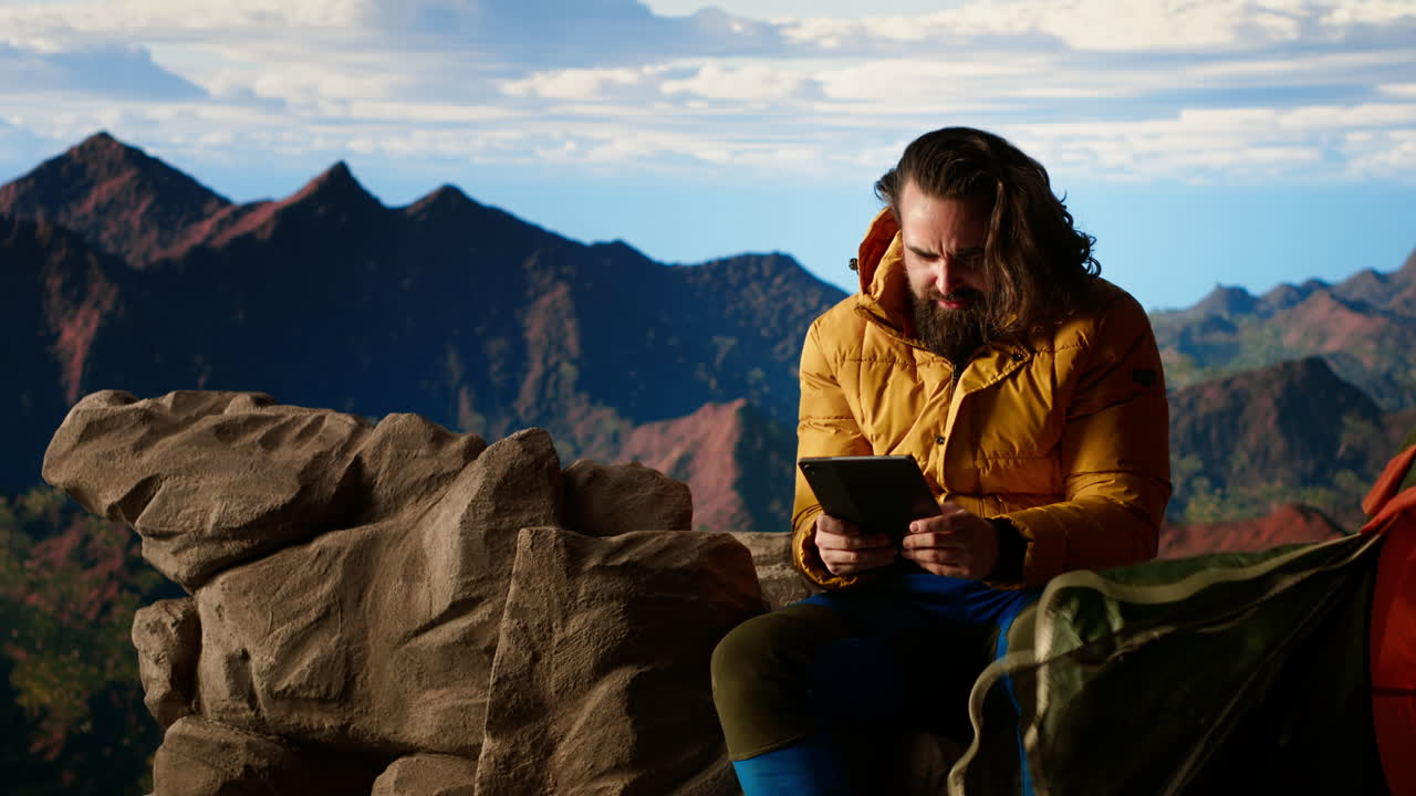 excursionista masculino lucha para trabajar en línea en condiciones de viento en el pico de la montaña remota