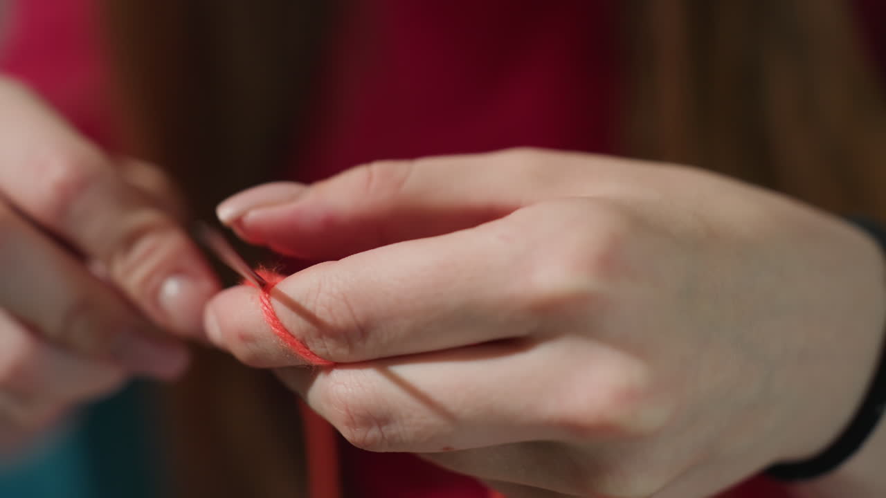 Una mujer crea hábilmente bucles rojos; una señora concentrada elabora con precisión pequeños círculos de lana; su rostro revela una intensa concentración mientras crea con destreza círculos de punto en miniatura con hilo rojo vibrante.