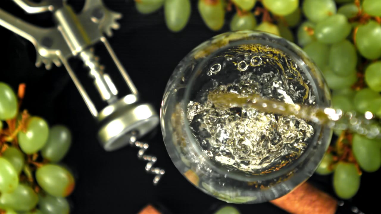 Versamento dall'alto in movimento rallentato di vino bianco in un bicchiere con uva