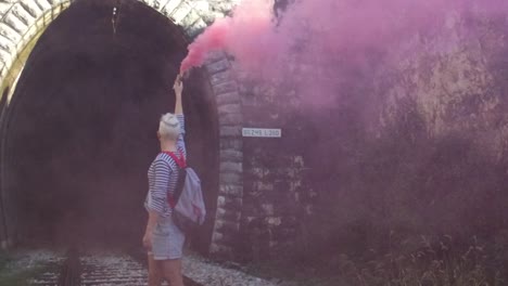 person releasing pink smoke in a tunnel near train tracks