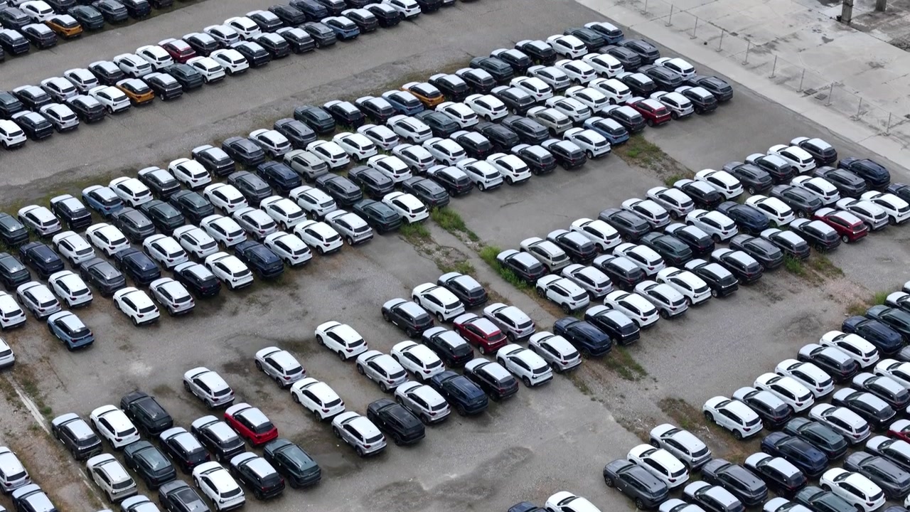 Cientos de vehículos de pasajeros están estacionados en filas organizadas en un gran patio de almacenamiento automotriz, destacando estilos de carrocería de vehículos mixtos, gestión de inventario y operaciones logísticas (vista aérea).