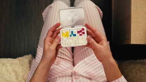 person in pink pajamas holding pill organizer