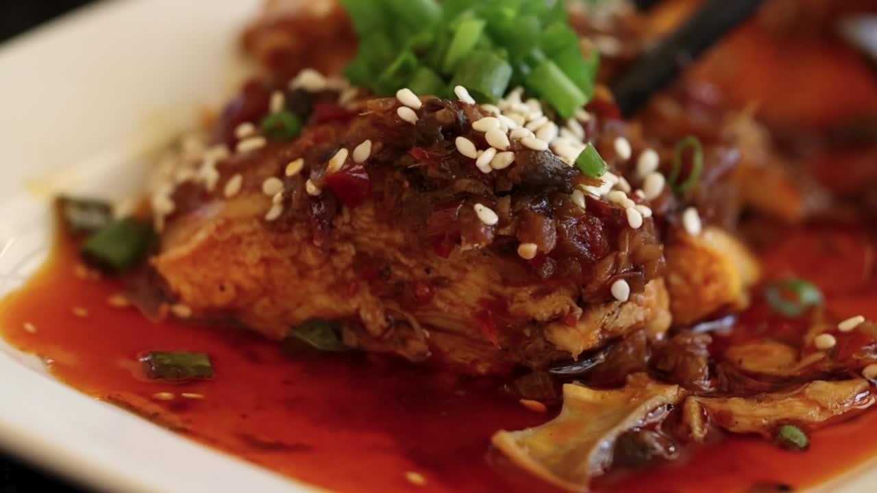 Close-up of a spicy dish topped with sesame seeds and green herbs, served in a vibrant red sauce.
