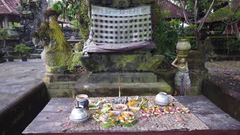 balinese hindu offerings in masceti temple entrance, praying flowers, incense, dragon statues and a holy tree at the gate of the spiritual compound for praying and worshiping, bali, indonesia