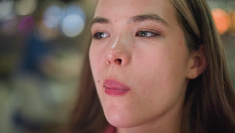 close-up of a woman enjoying a french fry with a subtle smile on her face with spots on her face , enjoying the delicious taste of the french chops, with blur soft colored light in the background